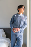 Person wearing a light blue sweatshirt and pants in a bedroom setting.