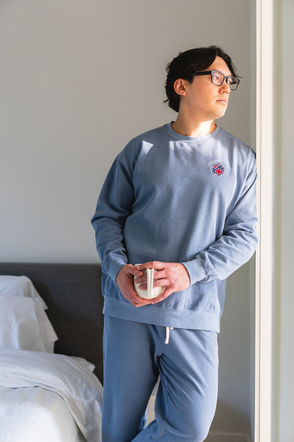 Person wearing a light blue sweatshirt and pants in a bedroom setting.