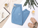 Blue sweatpants with 'Post Shift' text on a white surface with a cup, book, and slippers.