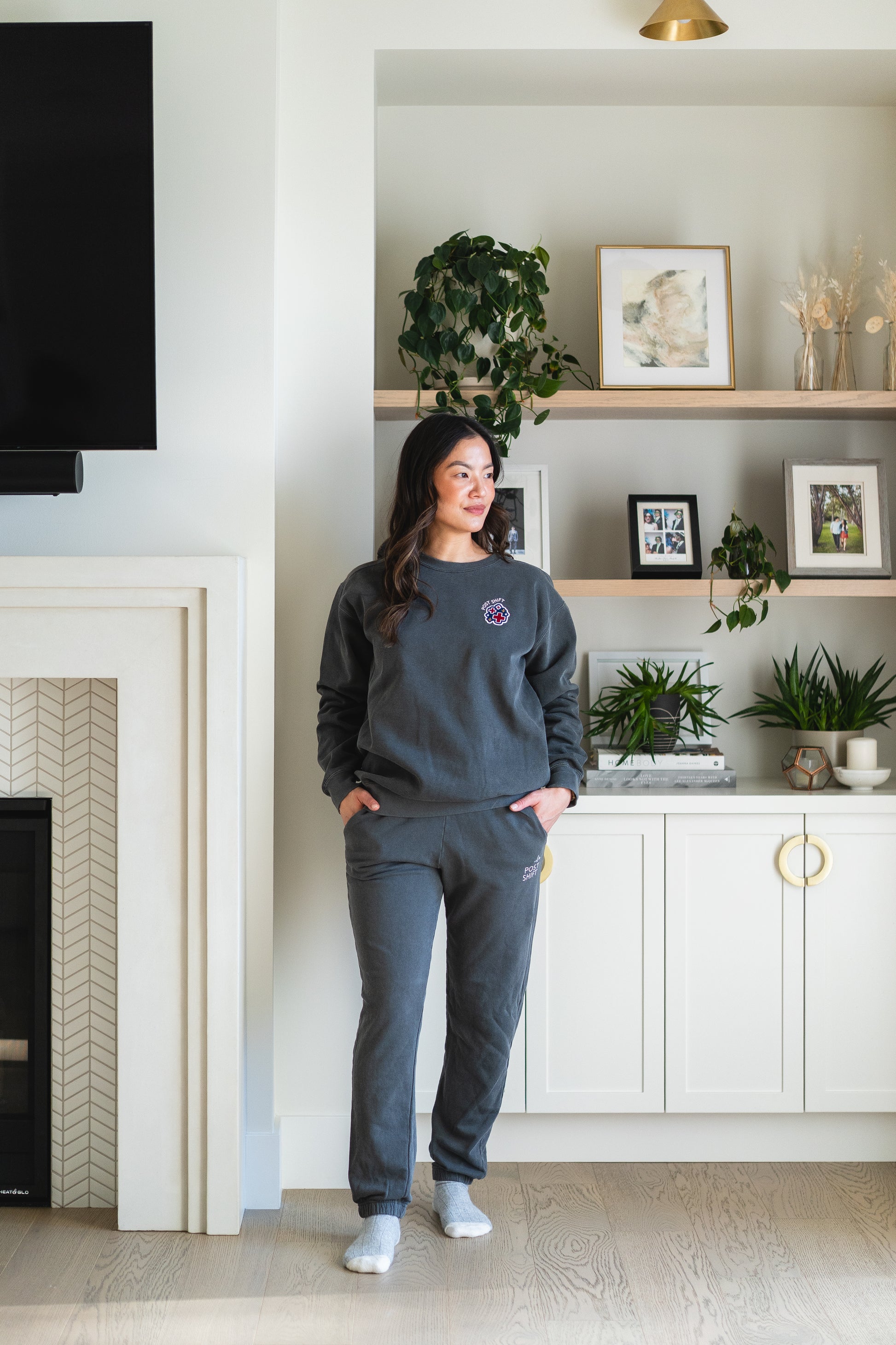 Person wearing a dark gray sweatshirt and pants in a living room with white walls and decorative elements.